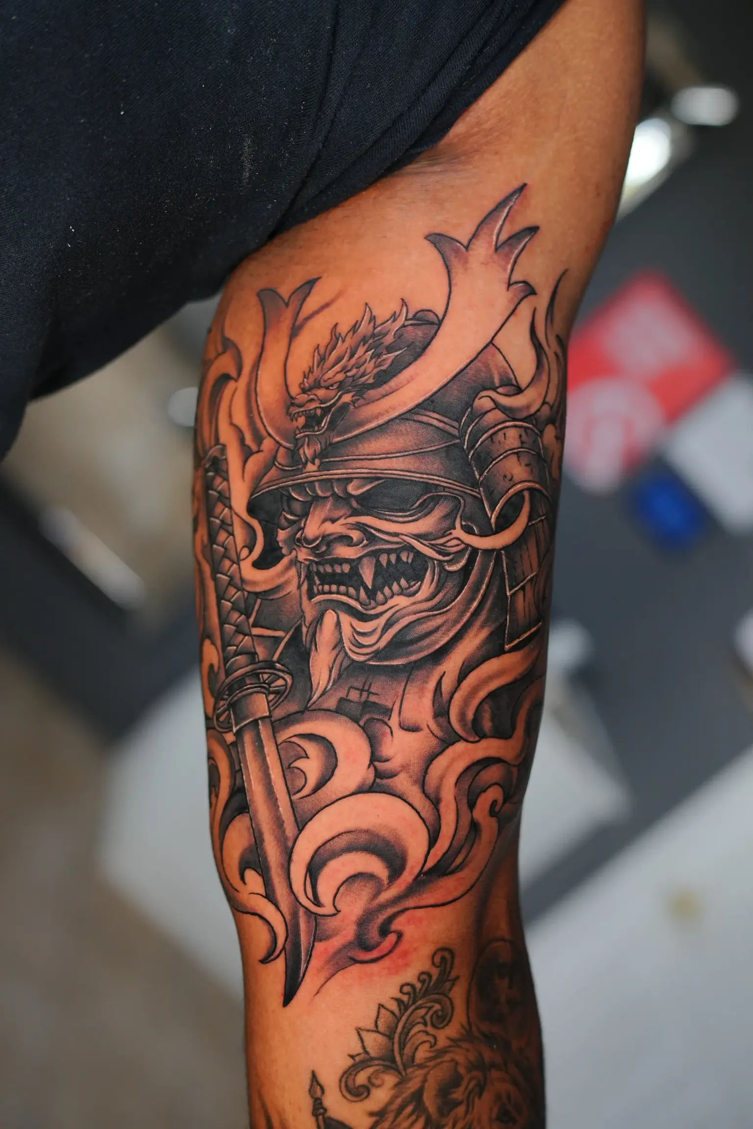 Black and grey samurai mask tattoo with dragon detail and sword on the forearm