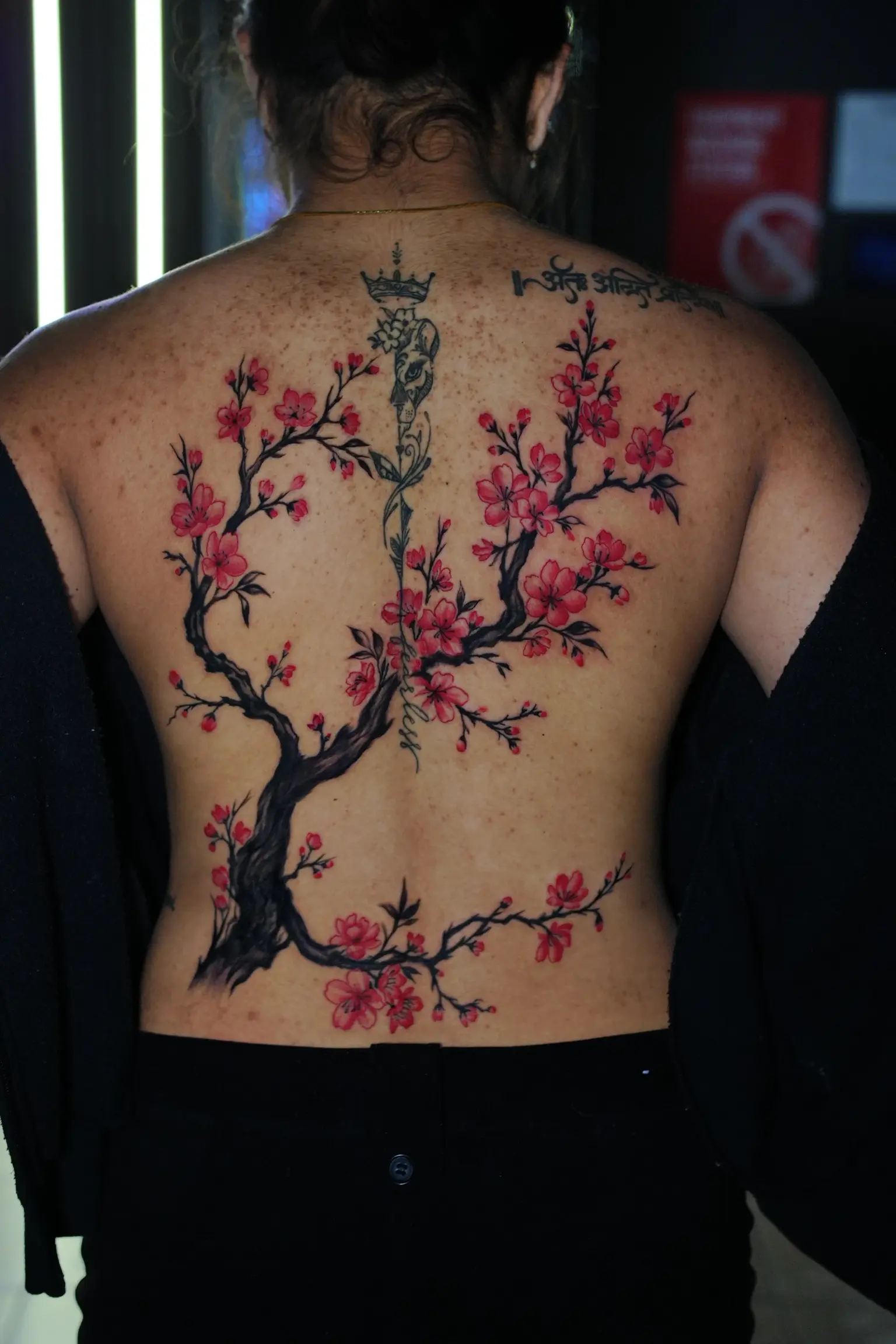 Vibrant red cherry blossom branch tattoo cascading down back and spine with fine-line script