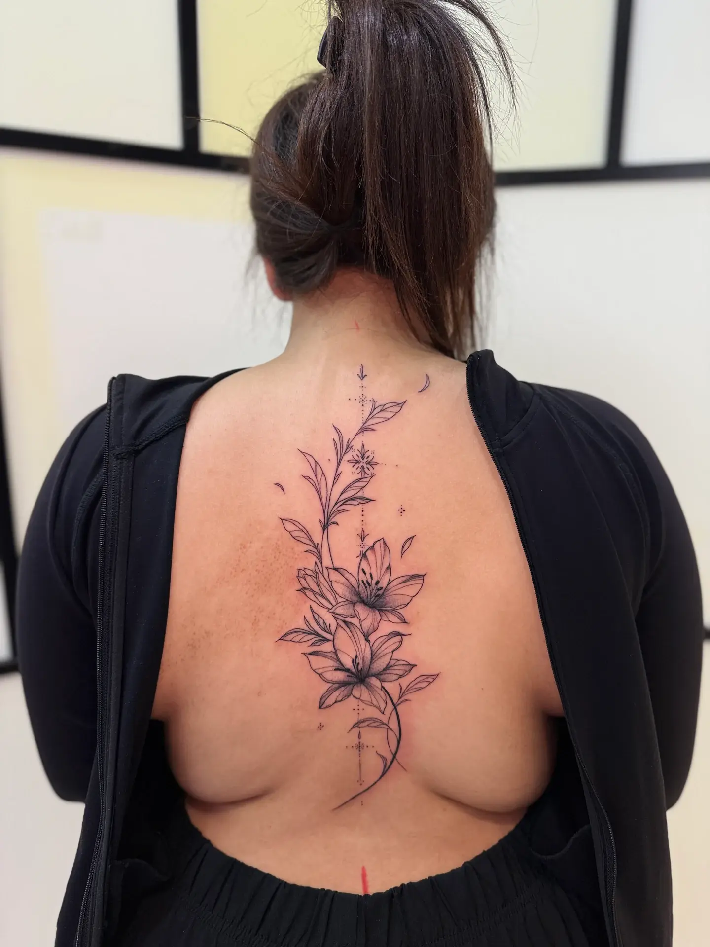 Delicate fine line lily flower tattoo running down spine